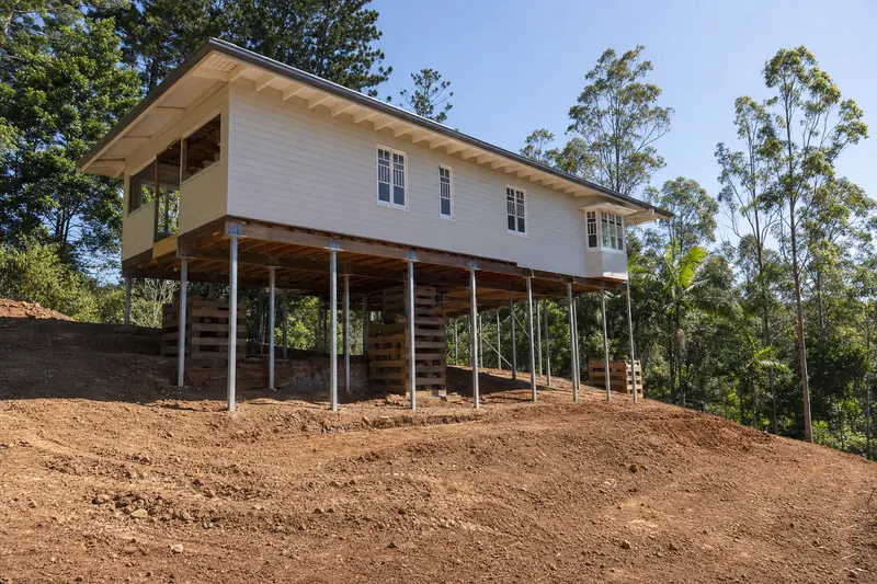 Hardwood Queenslander raised on tall steel posts and hardwood cribbing on a sloping hinterland block with deep red basalt soil, illustrative example