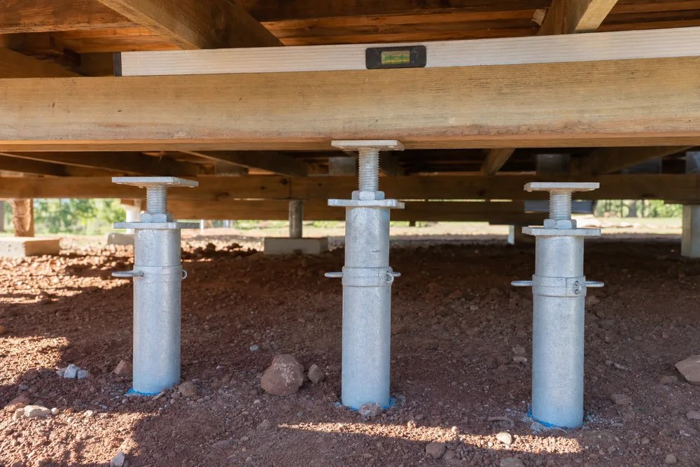 Adjustable steel stumps under a timber floor frame, one wound higher than its neighbours with a spirit level across the bearer, illustrative example